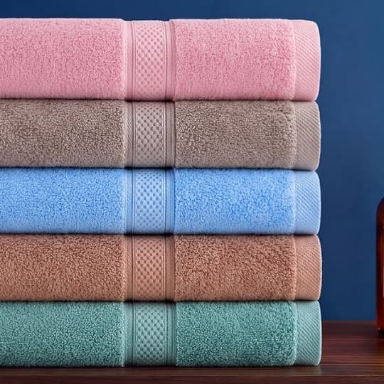 Năm chiếc khăn tắm Toweland nhiều màu xếp chồng trên kệ gỗ nền xanh navy.