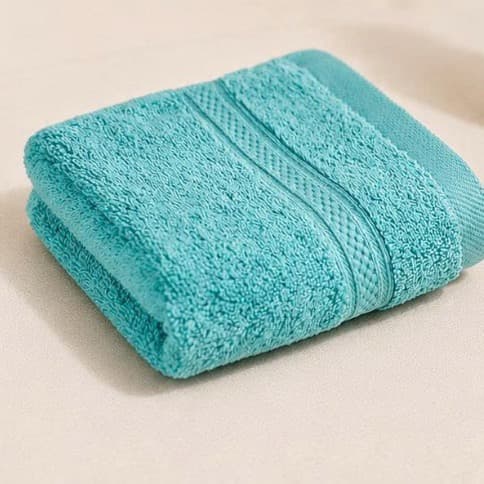 Khăn mặt tre Toweland màu xanh ngọc gấp gọn trên nền be.